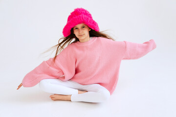 Excited girl model in pink hat posing in studio. Clothes, children's fashion concept. Positive child dancing in studio