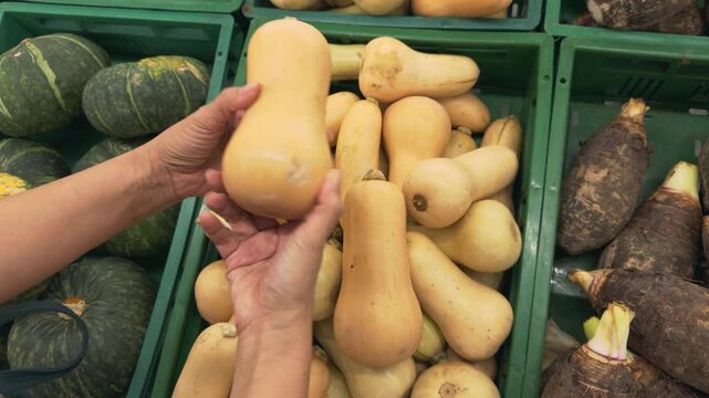 Woman hand choosing organic butternut squash from fresh produce display in supermarket, healthy eating lifestyle, fresh vegetables, autumn harvest, plant-based food, farm-to-table movement, nutrition
