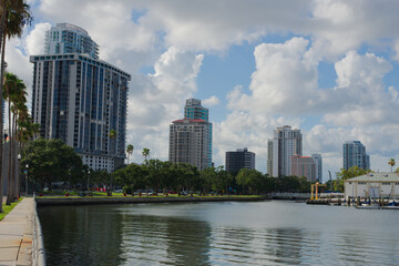 Obraz premium Modern Urban Scene with High Rise Buildings by Waterfront in Sunny Weather in St. Petersburg, FL. Picturesque view of urban high rise buildings along a tranquil waterfront near Tampa Bay, framed by gr