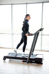 Young woman exercising on a treadmill in modern gym, focusing on health and fitness goals with...