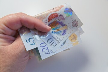 Holding polymer banknotes of five, ten, and twenty pounds in hand, highlighting the vibrant colors...