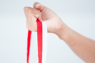 Hand Holding Red And White Striped Ribbon Against Light Gray Background