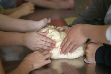 Children knead raw dough at a master class on making buns.
Children's hands touch raw dough