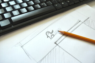 Top view of a pencil sketch on paper with a small cartoon character, placed beside a keyboard and...