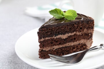Piece of delicious chocolate cake with mint and fork on grey table, closeup