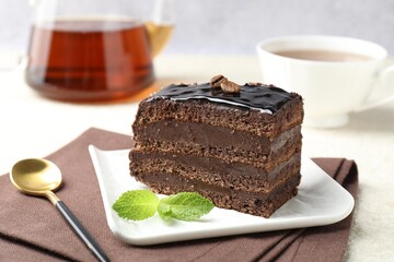 Piece of chocolate cake served with mint, spoon and tea on white table, closeup