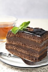 Piece of chocolate cake served with mint, fork and tea on table, closeup