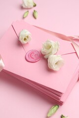 Stack of love letters and flowers on pink background, above view