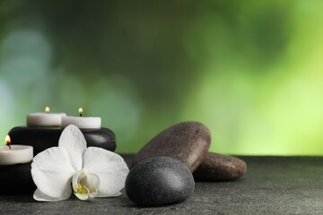 Spa stones, burning candles and orchid flower on grey table, closeup. Space for text