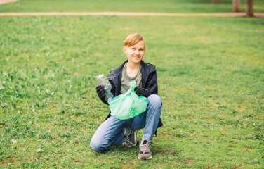 Teenager kid boy picking up trash plastic bottles in the park. Volunteer concept. Ecology,...