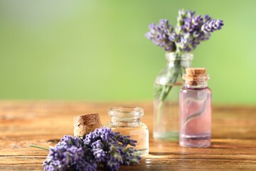 Bottles of lavender essential oil and flowers on wooden table, closeup. Space for text