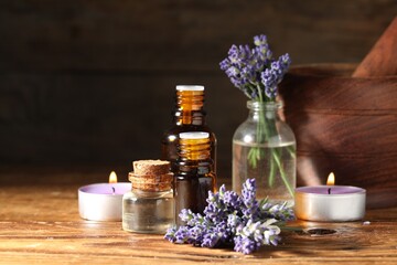 Bottles of lavender essential oil, burning candles and flowers on wooden table, closeup