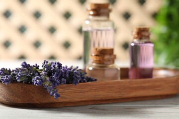 Bottles of essential oil and flowers on white wooden table, closeup