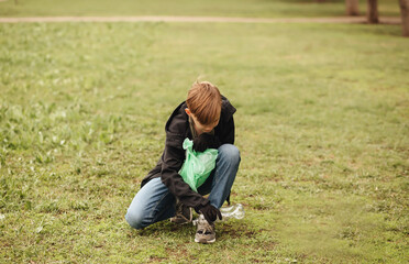 Teenager kid boy picking up trash plastic bottles in the park. Volunteer concept. Ecology,...