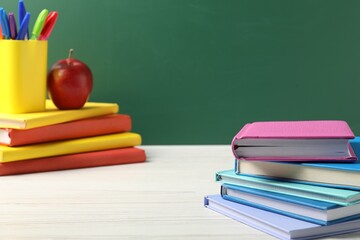 Different school stationery and red apple on white wooden table against blackboard, closeup