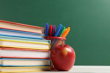 Different school stationery and red apple on white wooden table against blackboard, closeup. Space...