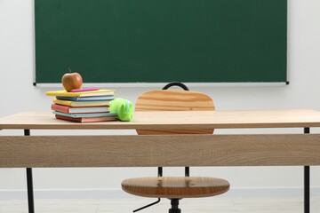 Different school stationery and apple on wooden table near blackboard indoors