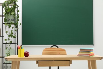 Different school stationery and red apple on wooden table near blackboard indoors