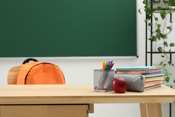 Different school stationery and red apple on wooden table near blackboard indoors