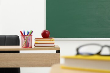 Different school stationery and red apple on wooden table near blackboard indoors