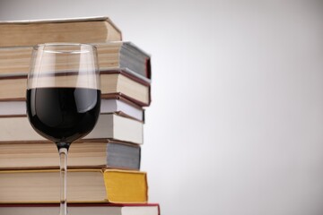 Red wine in glass and stack of books on light background, closeup. Space for text