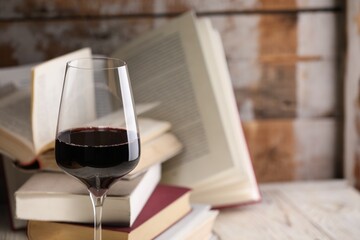 Red wine in glass and books on light table against color wooden background, closeup. Space for text