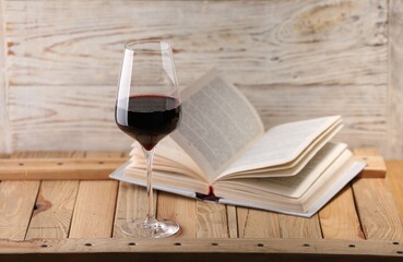 Red wine in glass and book on wooden table against light background, closeup