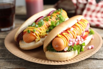 Delicious hot dogs with sauces, lettuce and onion on wooden table, closeup