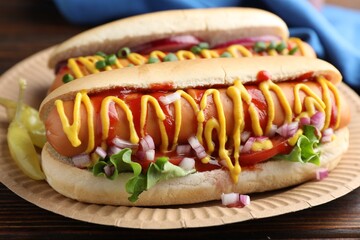Delicious hot dogs with sauces, lettuce and onion on wooden table, closeup