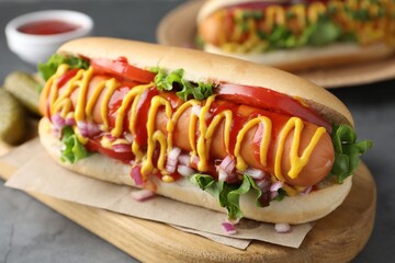Delicious hot dog with sauces, lettuce, onion and tomato on grey textured table, closeup