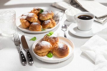 Appetizing profiteroles with custard in a white plate on the table. Eclairs, coffee, dessert.