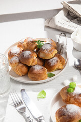 Appetizing profiteroles with custard in a white plate on the table. Eclairs, coffee, dessert.