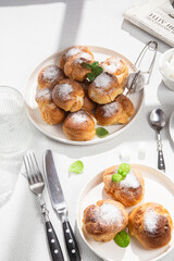 Appetizing profiteroles with custard in a white plate on the table. Eclairs, coffee, dessert.