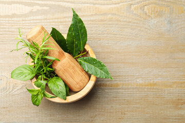 Different aromatic herbs in mortar on wooden table, top view. Space for text