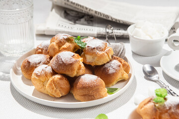 Appetizing profiteroles with custard in a white plate on the table. Eclairs, coffee, dessert.