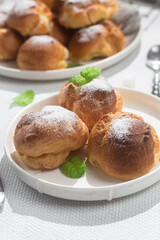 Appetizing profiteroles with custard in a white plate on the table. Eclairs, coffee, dessert.