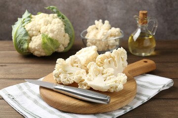 Fresh raw cauliflower florets, knife and oil on wooden table, closeup