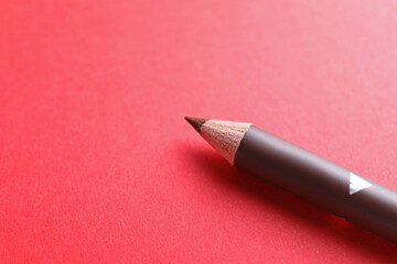 One eyebrow pencil on red background, closeup. Space for text