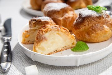 Appetizing profiteroles with custard in a white plate on the table. Eclairs, coffee, dessert.