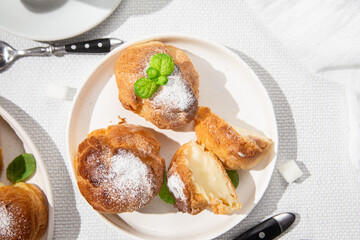Appetizing profiteroles with custard in a white plate on the table. Eclairs, coffee, dessert.