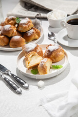 Appetizing profiteroles with custard in a white plate on the table. Eclairs, coffee, dessert.