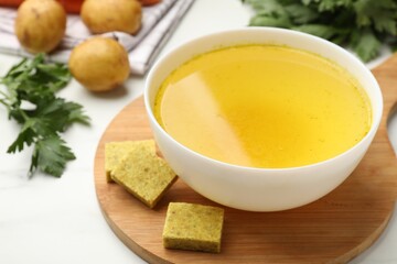 Aromatic bouillon cubes, broth, parsley and vegetables on white table, closeup
