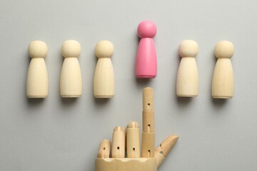 Unemployment. Hand figure pointing at pink figure among wooden on light background, flat lay