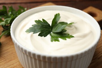 Tasty sour cream with parsley on wooden table, closeup