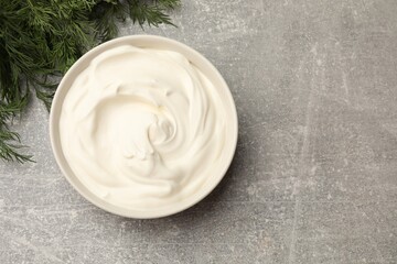 Tasty sour cream in bowl and dill on grey table, flat lay. Space for text