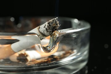 Cigarette butts in ashtray on black background, closeup