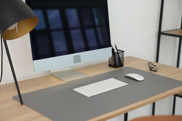 Stylish workplace with wooden desk, lamp and computer indoors, closeup