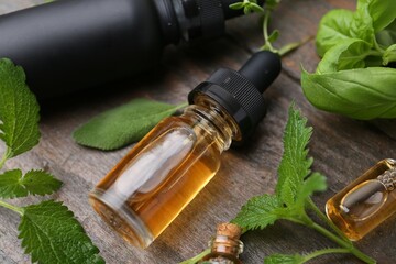Bottles of essential oil and herbs on wooden table, closeup