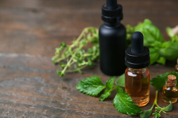 Bottles of essential oil and herbs on wooden table, closeup. Space for text