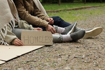 Poor people with sign Homeless on carton in park, closeup